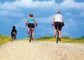 Man and woman riding bikes with dog running beside them