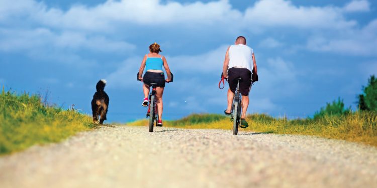 Man and woman riding bikes with dog running beside them