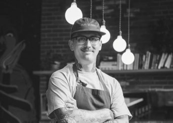Mark Bolton stands with his arms crossed inside the restaurant of Rolf and Daughters.