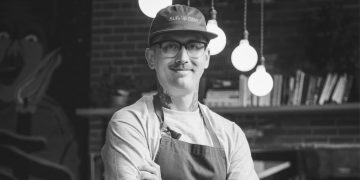 Mark Bolton stands with his arms crossed inside the restaurant of Rolf and Daughters.