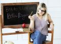 Model sits at a school desk in a purple top, jeans, and accessories from Bella Ragazza Boutique.