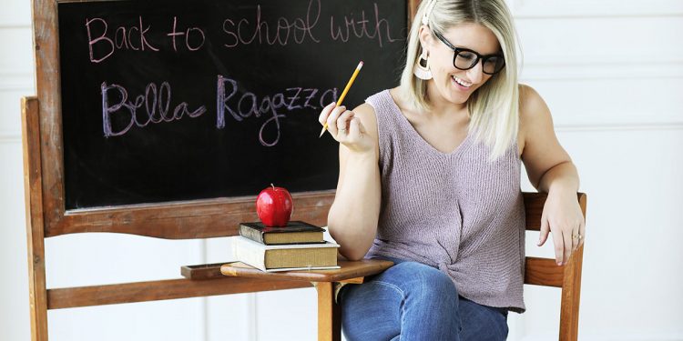 Model sits at a school desk in a purple top, jeans, and accessories from Bella Ragazza Boutique.