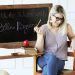 Model sits at a school desk in a purple top, jeans, and accessories from Bella Ragazza Boutique.