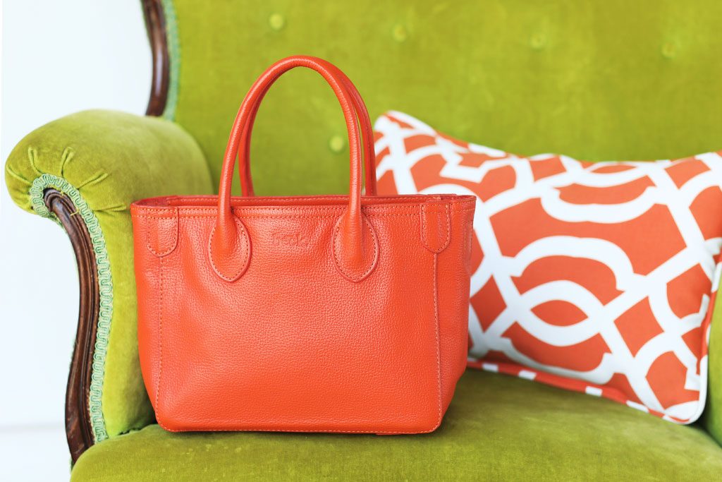 Orange purse sits on display in a green chair.