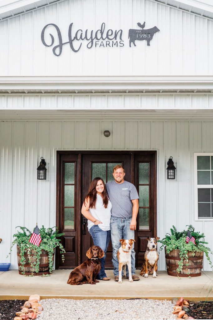 Danielle and Daniel Hayden stand smiling with their three dogs.