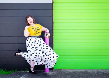 Mary Katherine Maddox, owner of M.porium, poses in a black and white polka dotted skirt, paint supplies in her hand, and a huge smile on her face.
